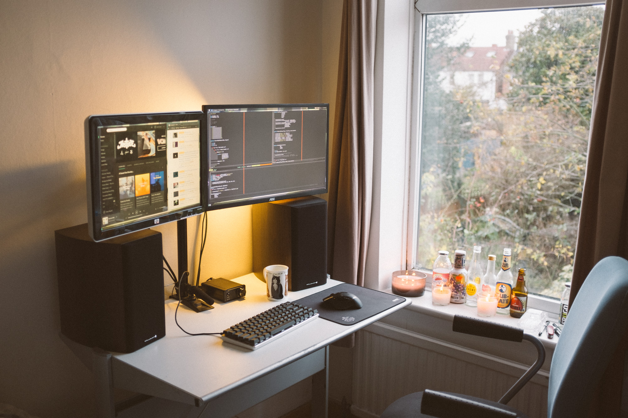 Picture of ikea desk with two large speakers and two monitors on a stand, the desk is quite cramped and next to a window